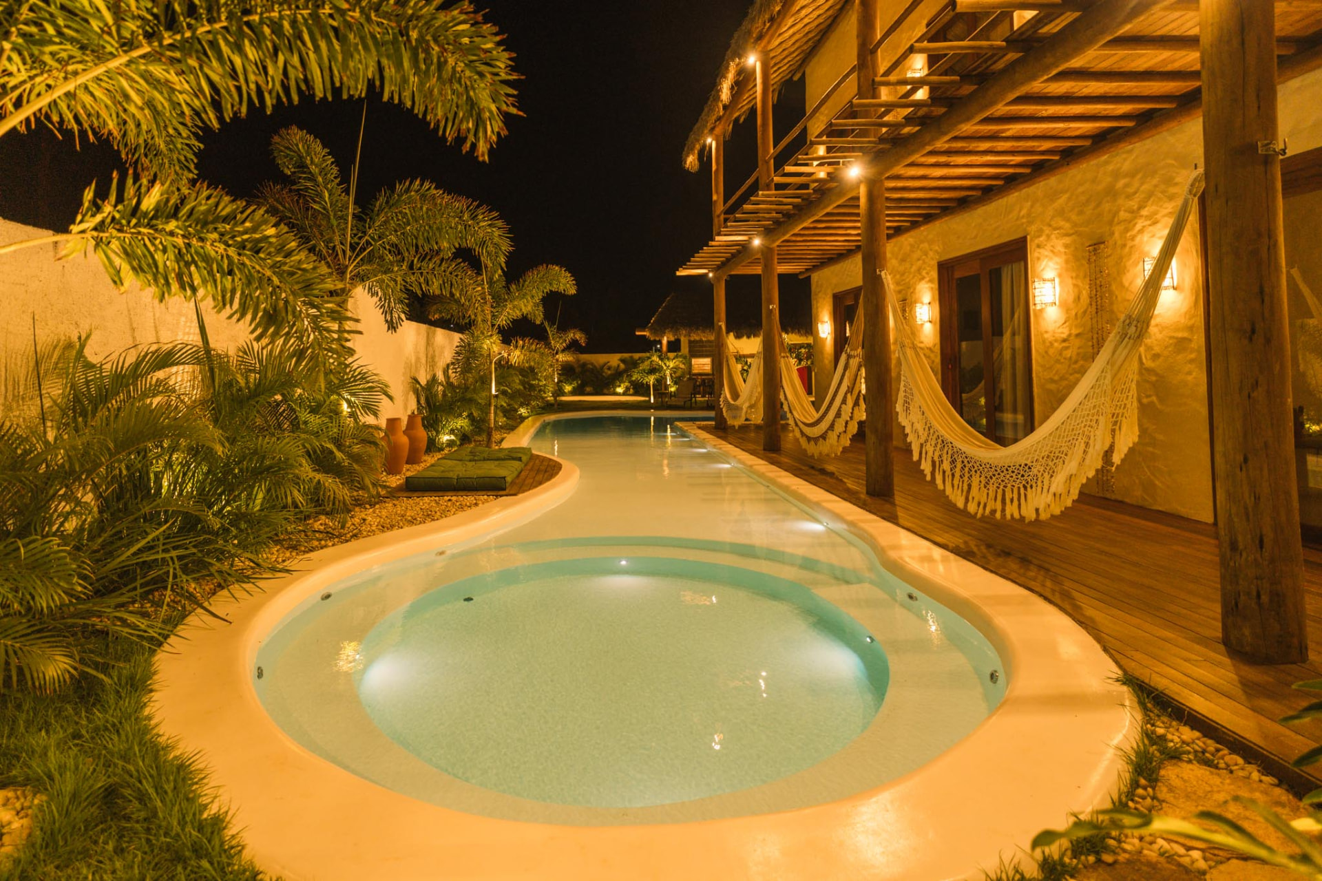Piscina e jacuzzi iluminadas à noite ao lado das redes da varanda